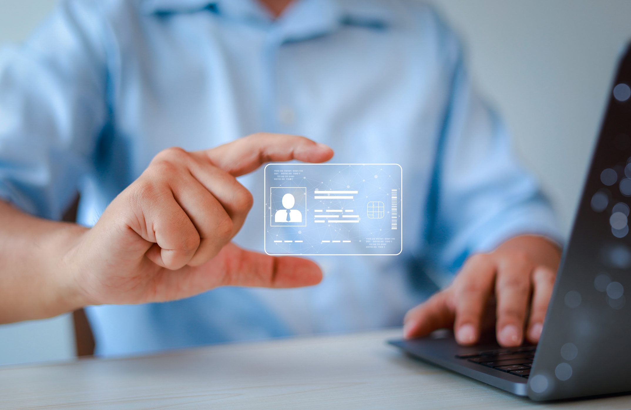 Person holding digital ID card near laptop.